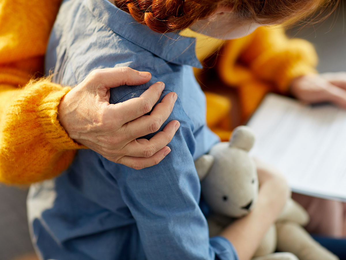 A child with an adult's arm around their shoulder