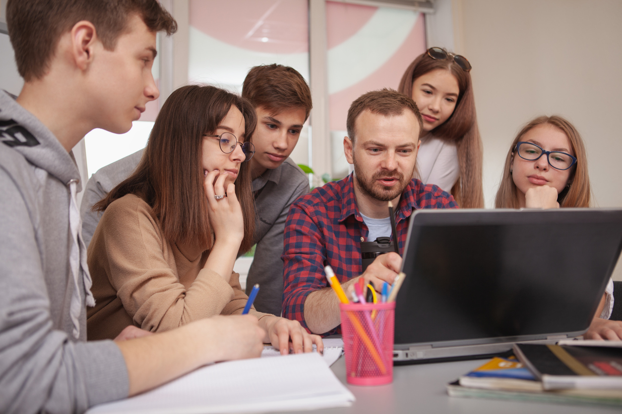 A teacher at a computer surrounded by pupils