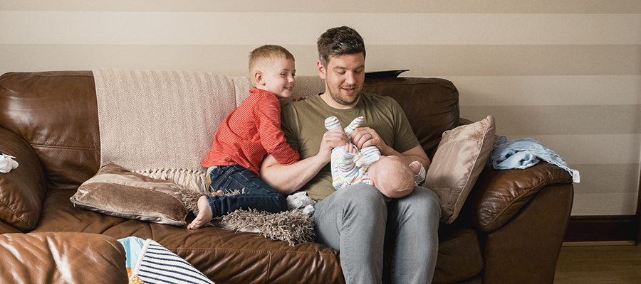 A father on a sofa with a young son and a baby