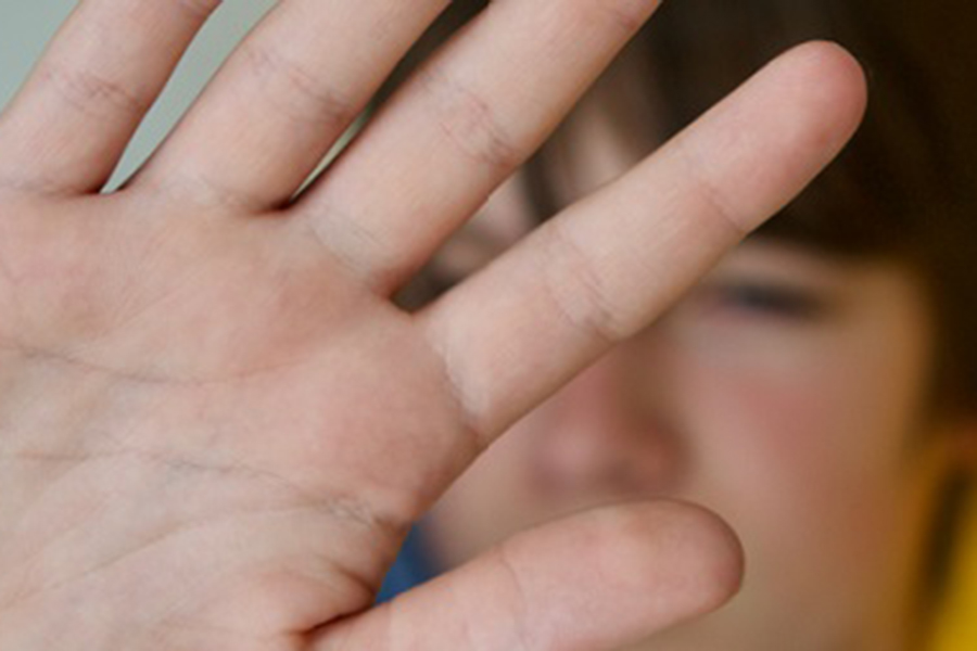 A young teen holding his hand in front of his face defensively