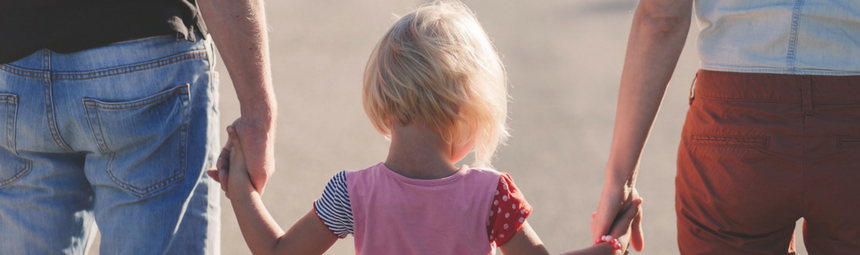 A child and two adults holding hands, walking away from the camera