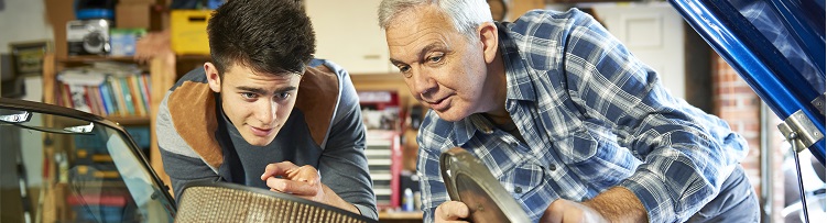 A teenager and an adult looking at a car engine