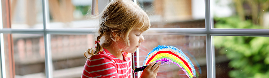 A young girl painting a rainbow on a window