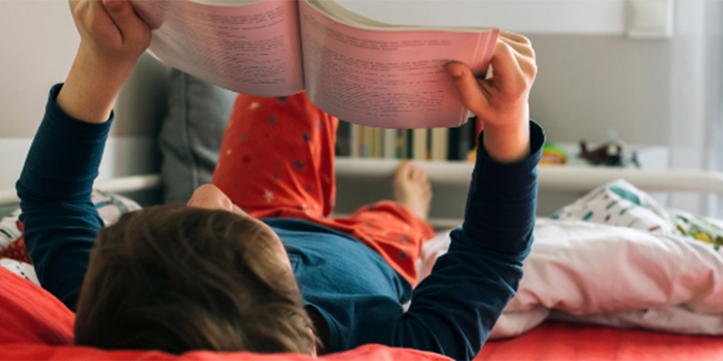 A child lying on a bed, reading a book