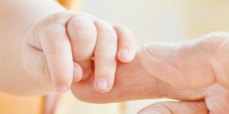 A baby's hand gripping an adults finger
