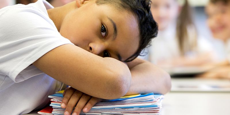 A school girl leaning on her work on a desk looking sad