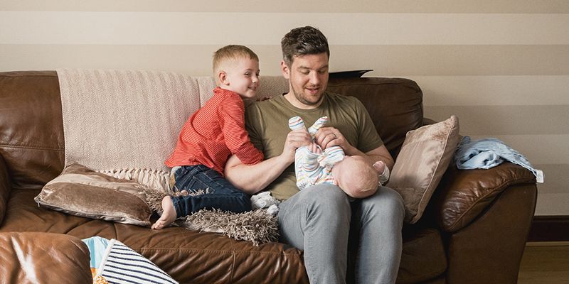 A father on a sofa with a young son and a baby