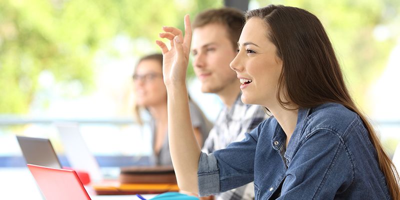 A student in class with her hand up to answer a question