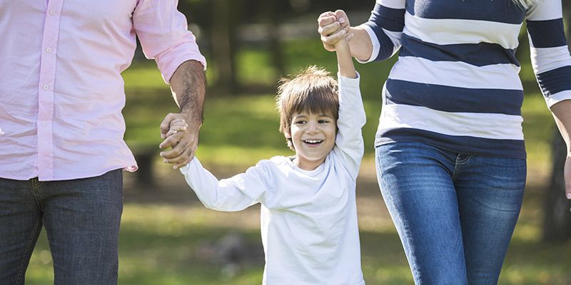 A happy child holding hands with two parents