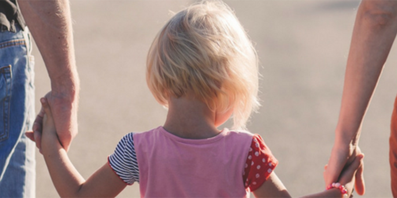 A child and two adults holding hands, walking away from the camera