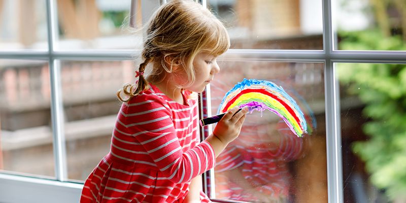 A girl painting a rainbow onto a window