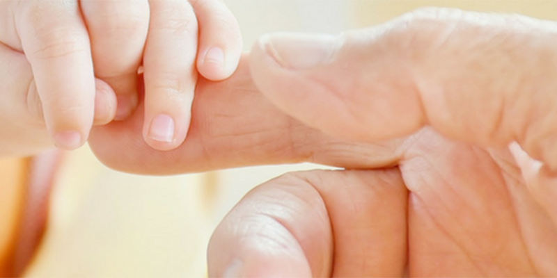 A baby's hand holding an adult's finger