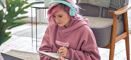 A teenager taking notes whilst working on a computer.