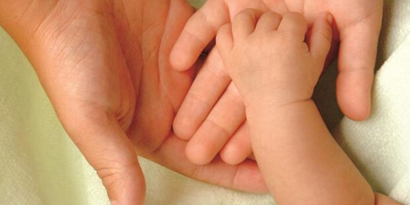 A small child's hand cupped by an adult's hand