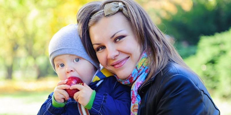 A mother holding a baby who is eating an apple